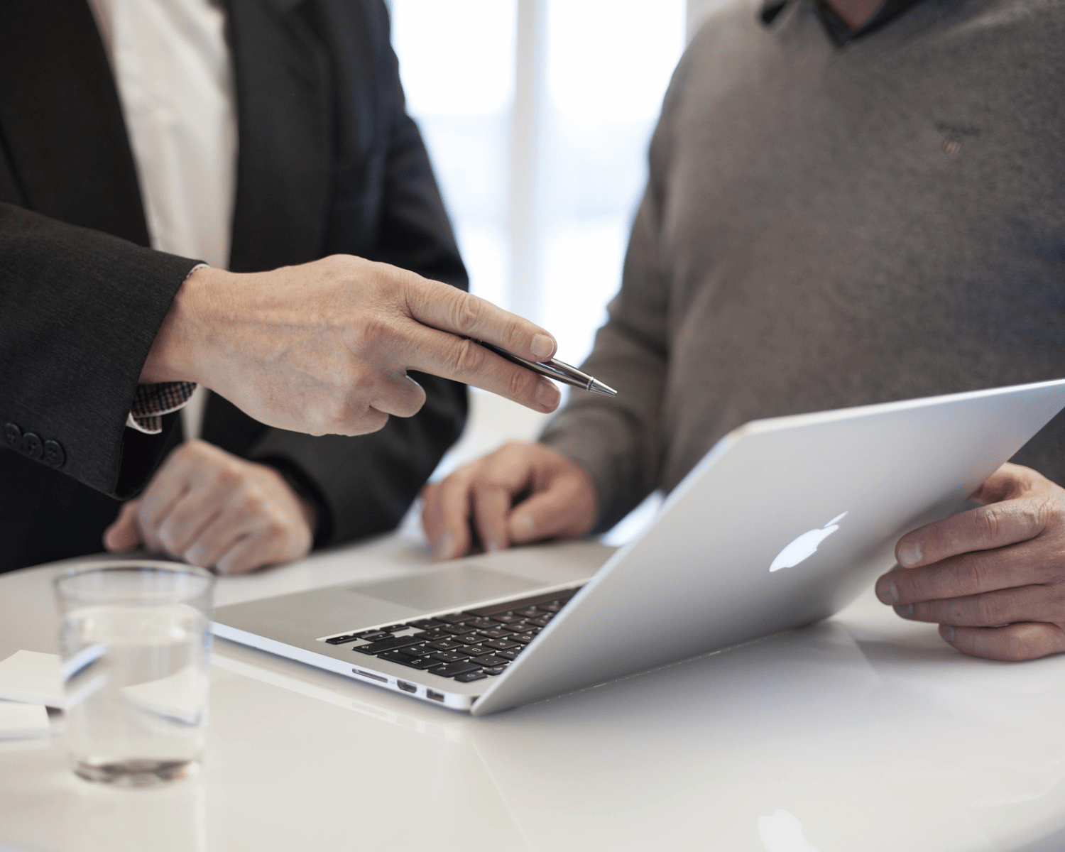 Zwei Business-Personen sitzen sich gegenüber und betrachten gemeinsam ein MacBook, während sie ein Beratungsgespräch führen.
